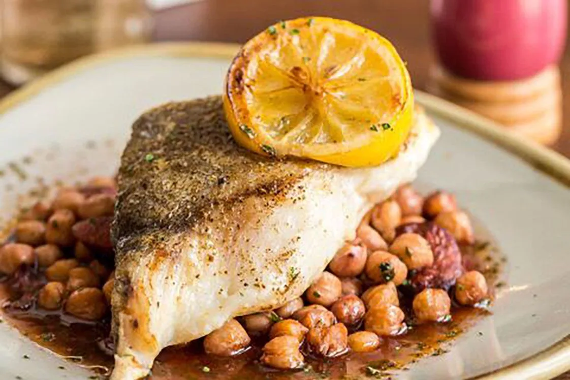 Baked cod fillet resting on herby chickpeas in a rustic baking dish