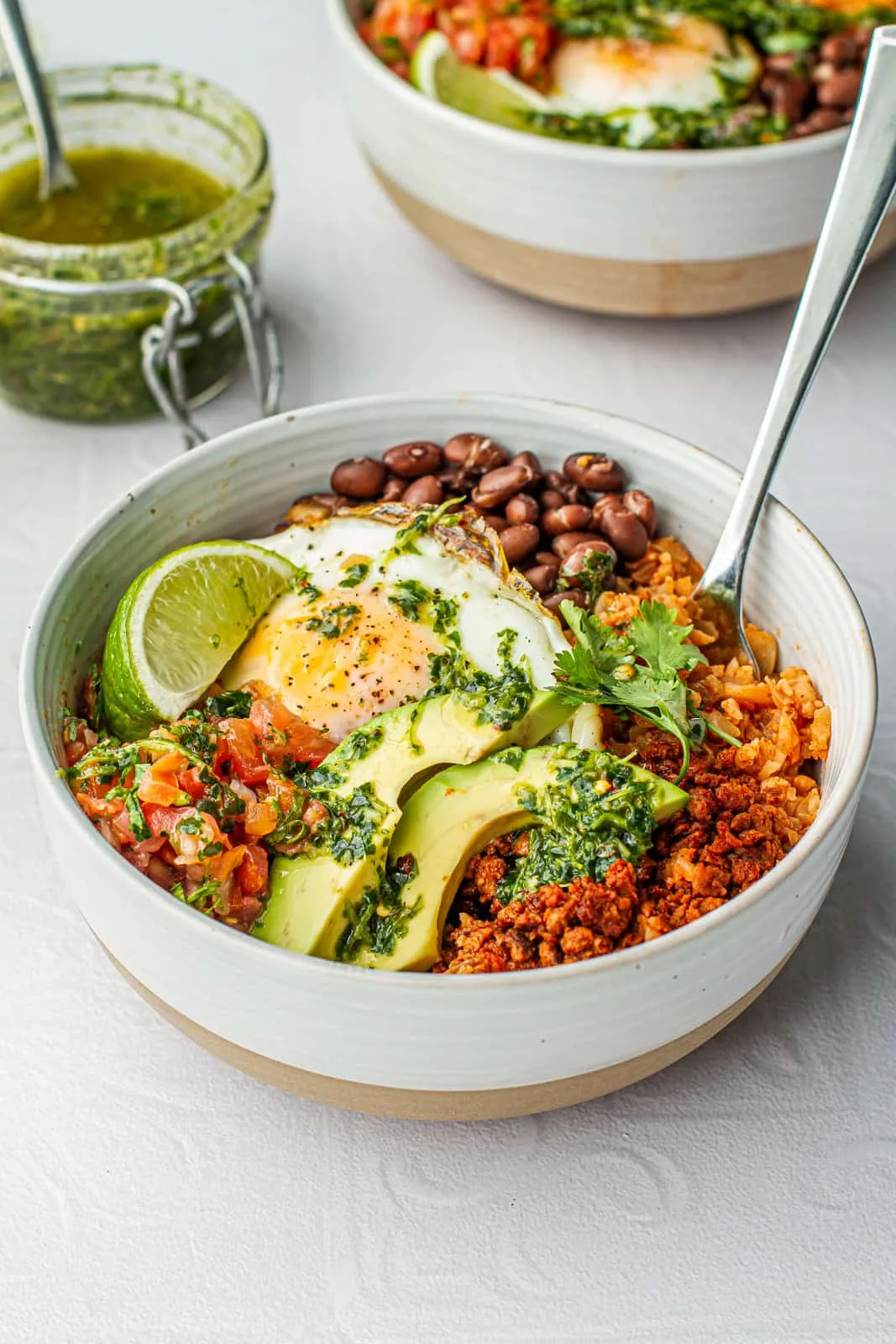 A burrito bowl with black beans, fried eggs, rice, and fresh toppings