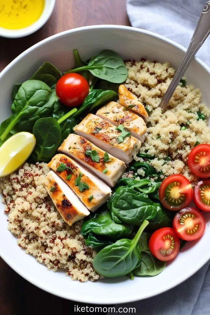 Grilled chicken slices over quinoa with roasted vegetables in a bowl