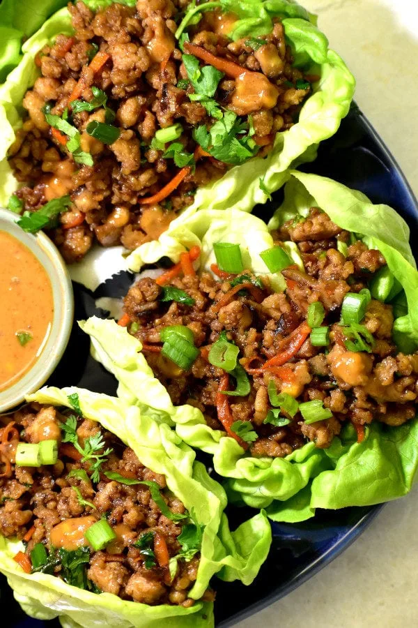 Chicken lettuce wraps drizzled with peanut sauce on a white plate