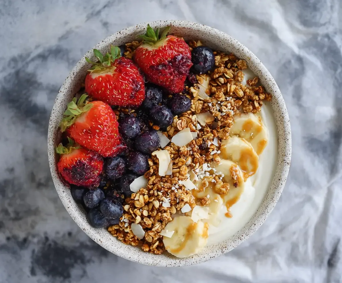 Greek yogurt topped with fresh mixed berries and granola in a white bowl