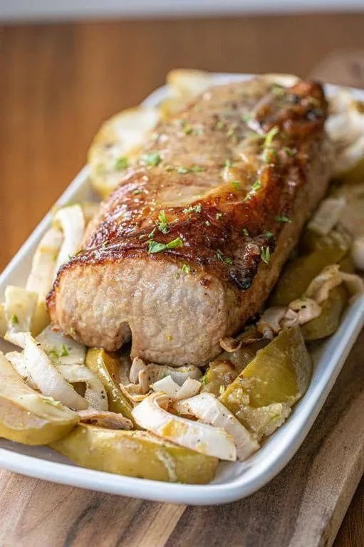 Sliced pork tenderloin with sautéed apples and mustard sauce on a white plate
