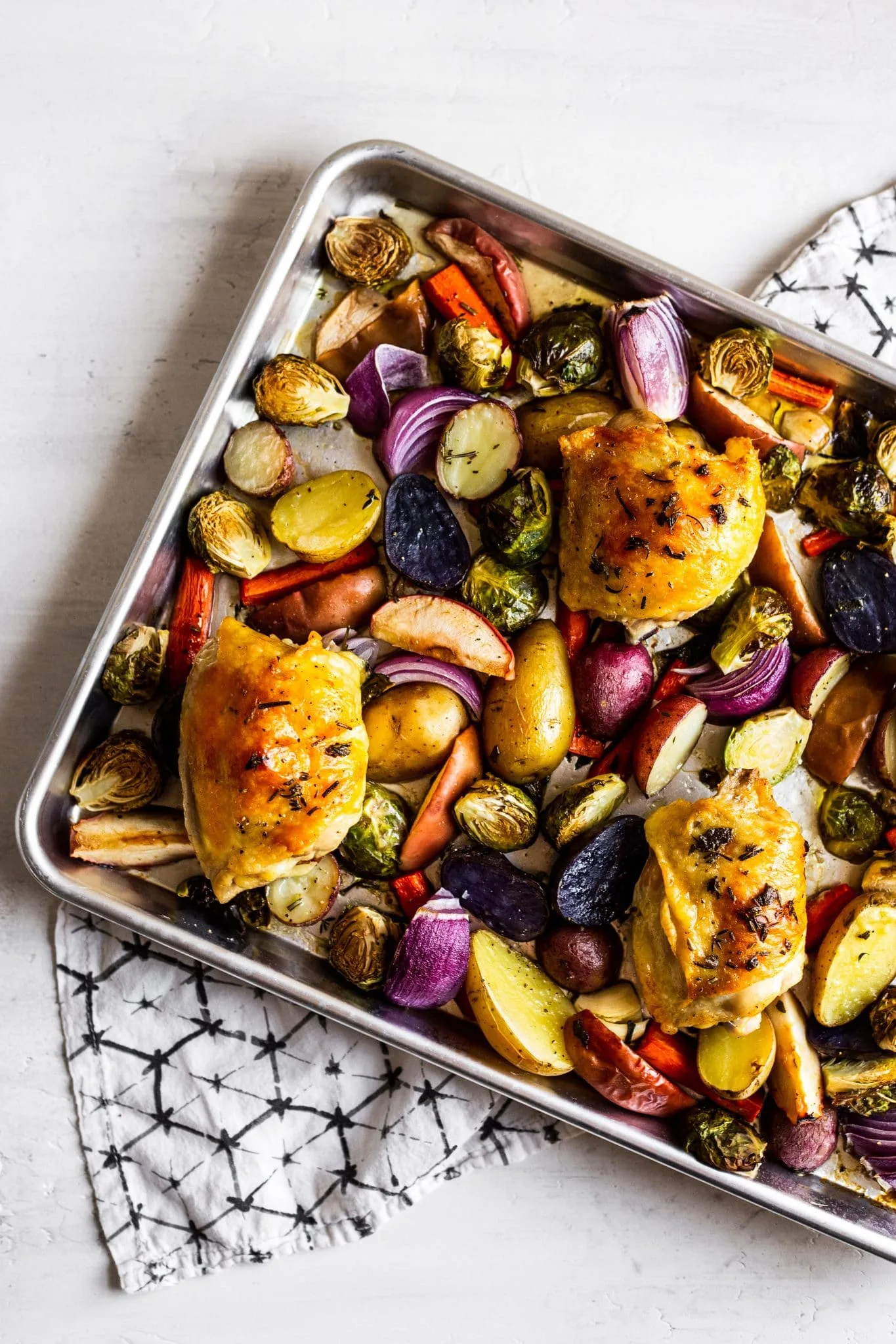 Golden roasted chicken thighs surrounded by colorful vegetables on a sheet pan