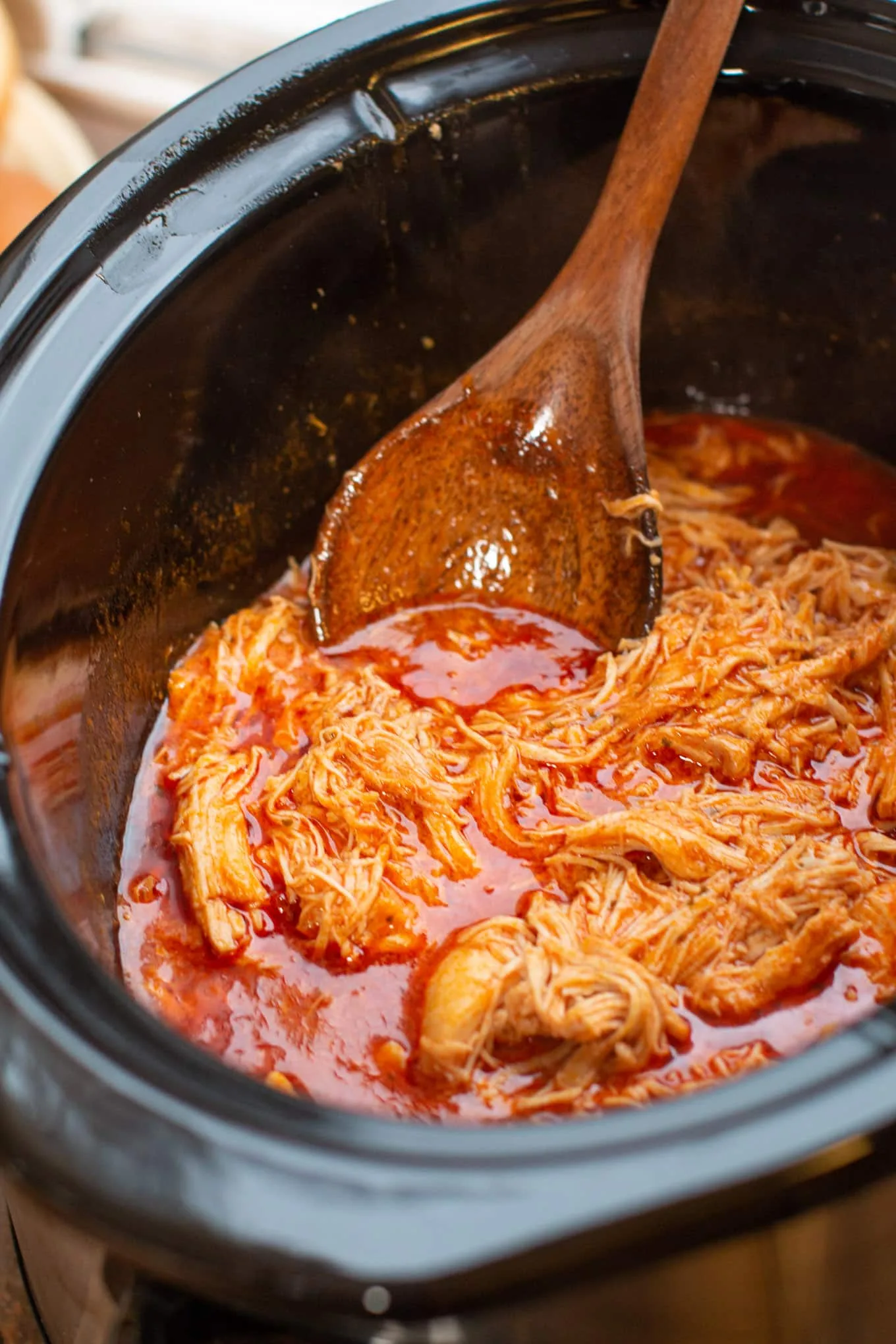 Shredded buffalo chicken in a slow cooker garnished with green onions