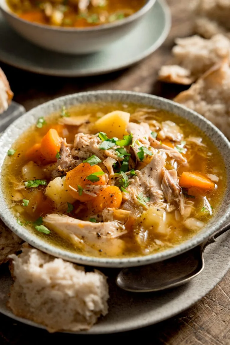 A hearty chicken bone broth soup with colorful vegetables in a white bowl