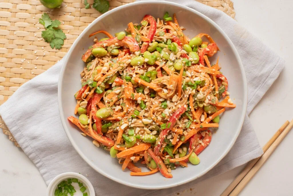Spicy peanut noodles topped with edamame and red chili flakes in a bowl